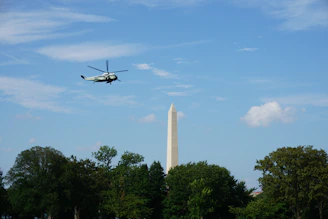 A helicopter flying smoothly over a green forest under a clear blue sky, symbolizing safety and environmental care.