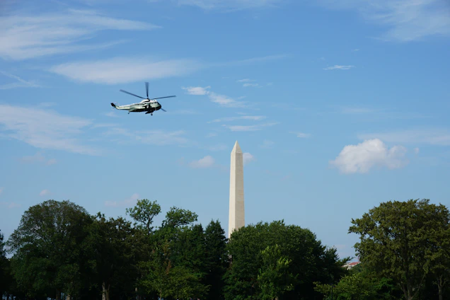 A helicopter flying smoothly over a green forest under a clear blue sky, symbolizing safety and environmental care.