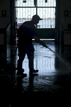 Silhouettes of two people cleaning a carpet with professional equipment in a bright room.