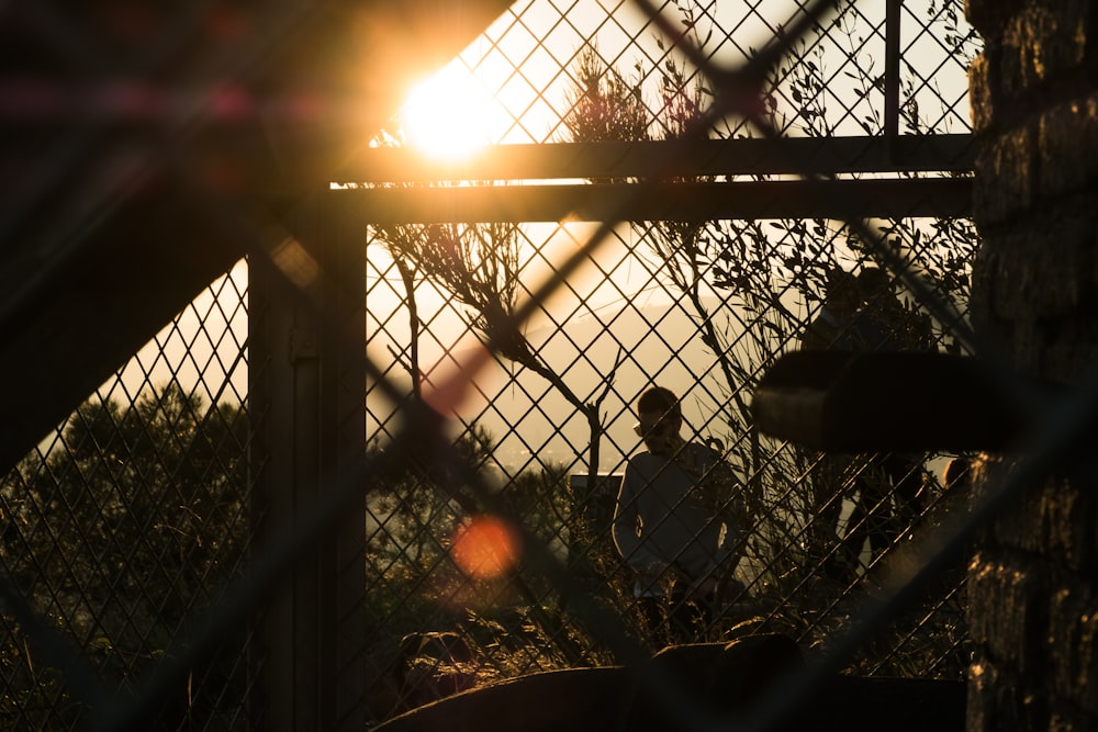 silhouette photography of man standing beside fence