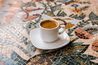 A steaming cup of coffee on a vintage ceramic saucer with a backdrop of traditional Mexican textiles.