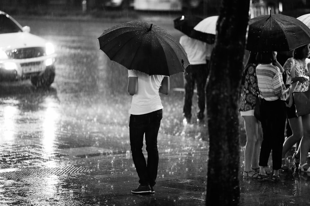 grayscale photography of people standing on road during rainy season