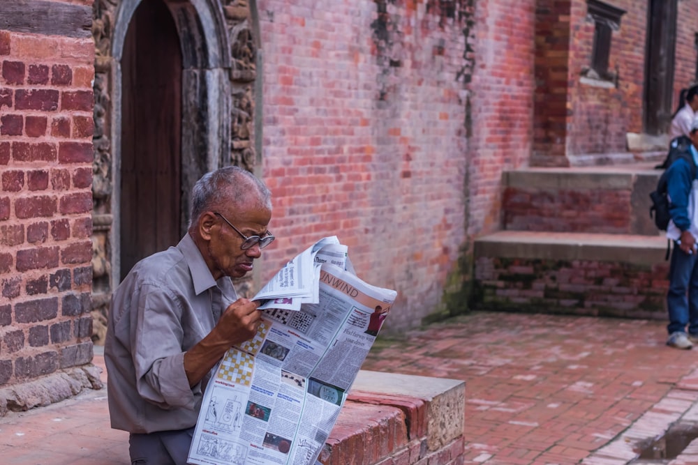man reading newspaper sitting on concrete bench