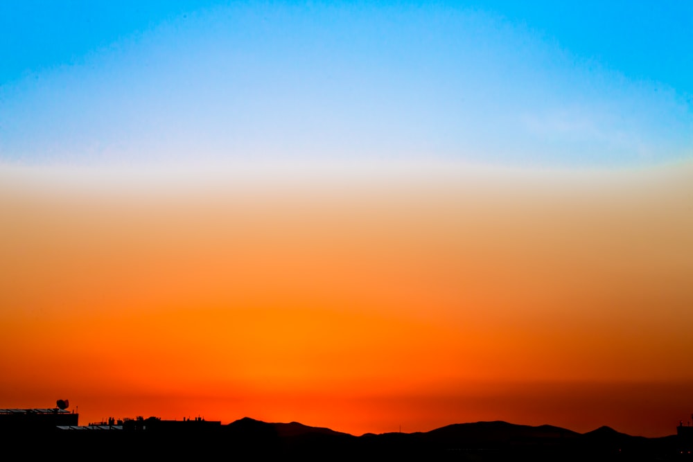 blue and orange sky and silhouette of hills wallpaper