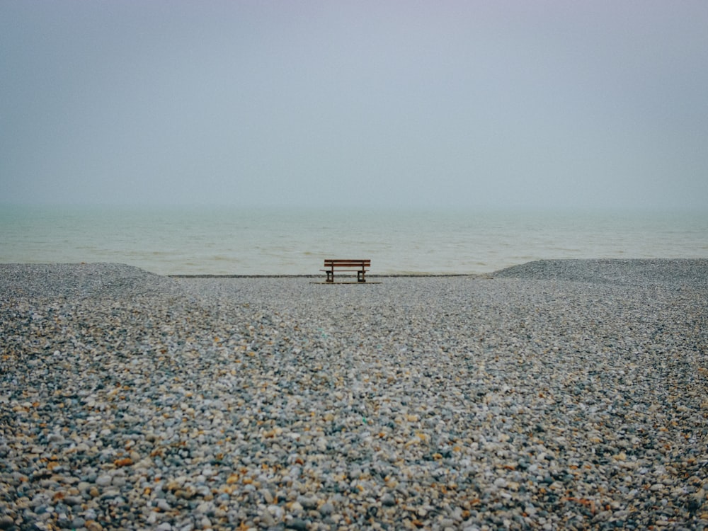 brown bench on rock near water under white clouds