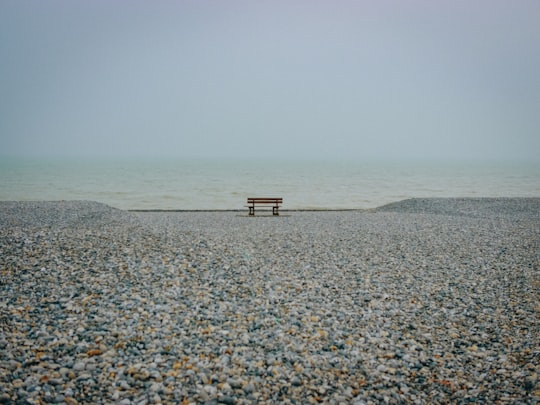 brown bench on rock near water under white clouds in Cayeux-sur-mer France