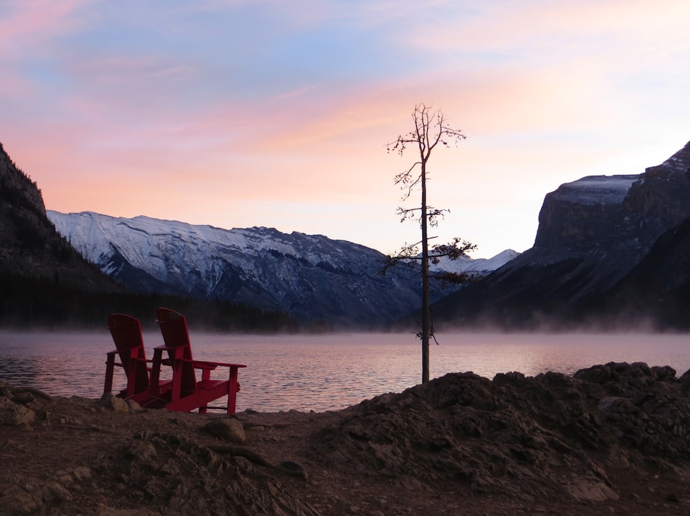 two red wooden adirondack chairs beside water