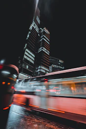 Futuristic electric buses and bikes moving through a sleek cityscape illuminated by teal and cyan lights.