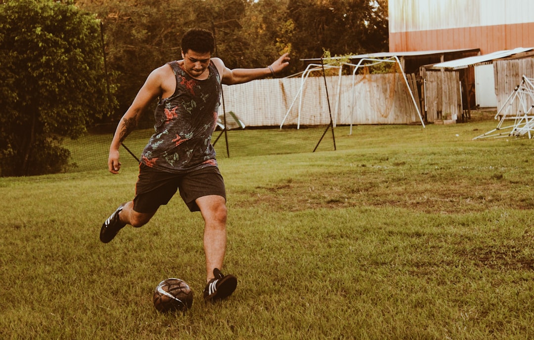 man kicking football on grass field during daytime