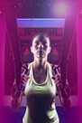 A person is using suspension trainers in a fitness environment. The lighting is dramatic, with a mix of bright and dark areas, creating a focused and intense atmosphere. The image captures the person's concentration and physical effort.