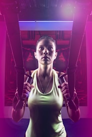 A person is using suspension trainers in a fitness environment. The lighting is dramatic, with a mix of bright and dark areas, creating a focused and intense atmosphere. The image captures the person's concentration and physical effort.