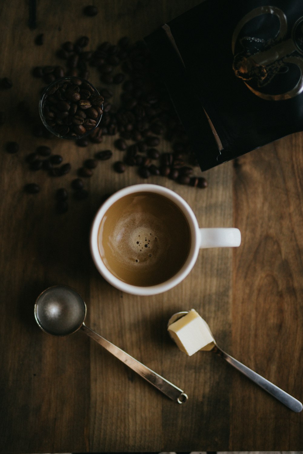 茶色の木製の表面にコーヒー豆とスプーンの横にあるコーヒーと白いセラミックカップ