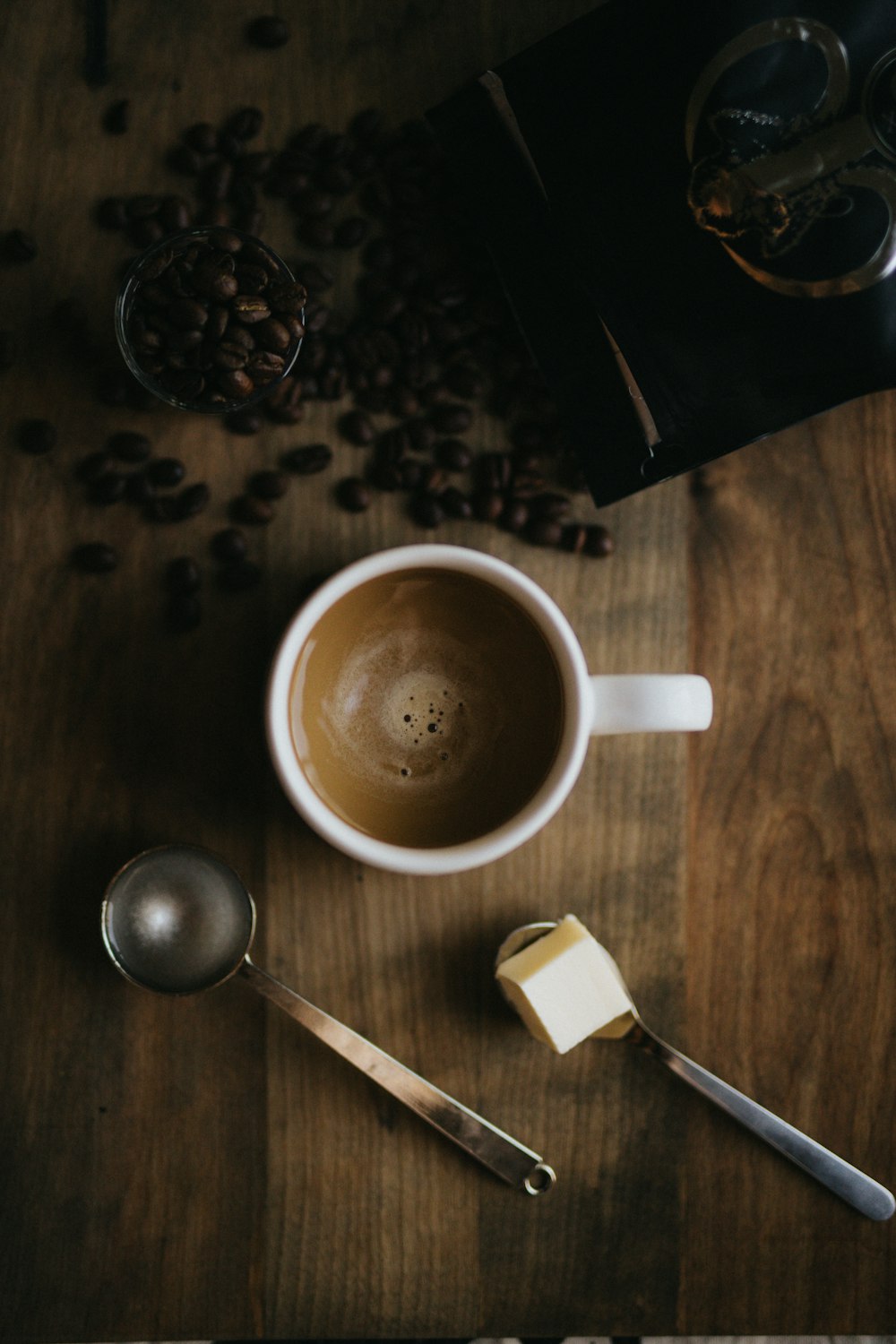 white ceramic cup with coffee beside coffee beans and spoon on brown wooden surface