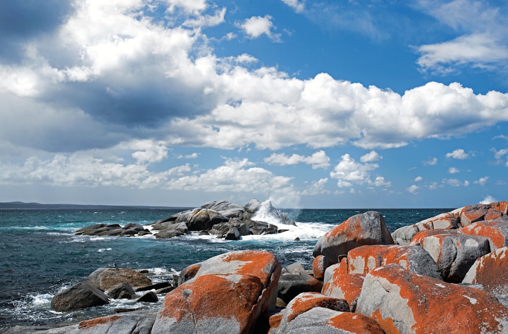 Welle plätschert auf Felsen unter weißem und blauem Himmel