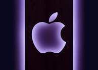 Apple logo glowing softly on a sleek black surface with futuristic neon accents.