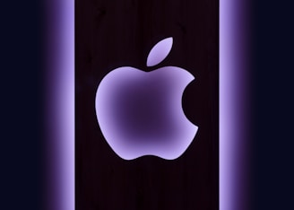 Apple logo glowing softly on a sleek black surface with futuristic neon accents.