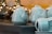White ceramic teapots and cups are neatly arranged on a table, with reflective surfaces creating soft highlights. The background showcases blurred, warm lighting from what appear to be glass objects or decor.