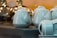 White ceramic teapots and cups are neatly arranged on a table, with reflective surfaces creating soft highlights. The background showcases blurred, warm lighting from what appear to be glass objects or decor.