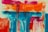 An abstract painting featuring vibrant colors with bold strokes. The top portion has vivid oranges and pinks, transitioning into blues and teals towards the bottom. The overall composition is dynamic and expressive with a combination of horizontal and vertical lines.