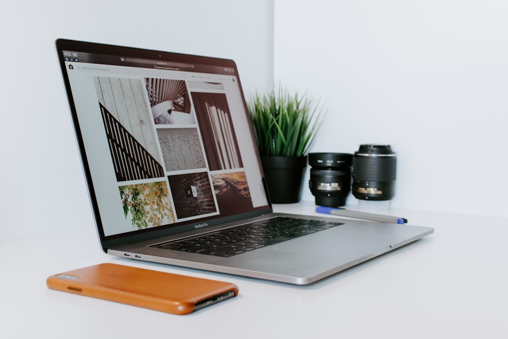 opened MacBook Air beside smartphone, potted plant, and camera lenses