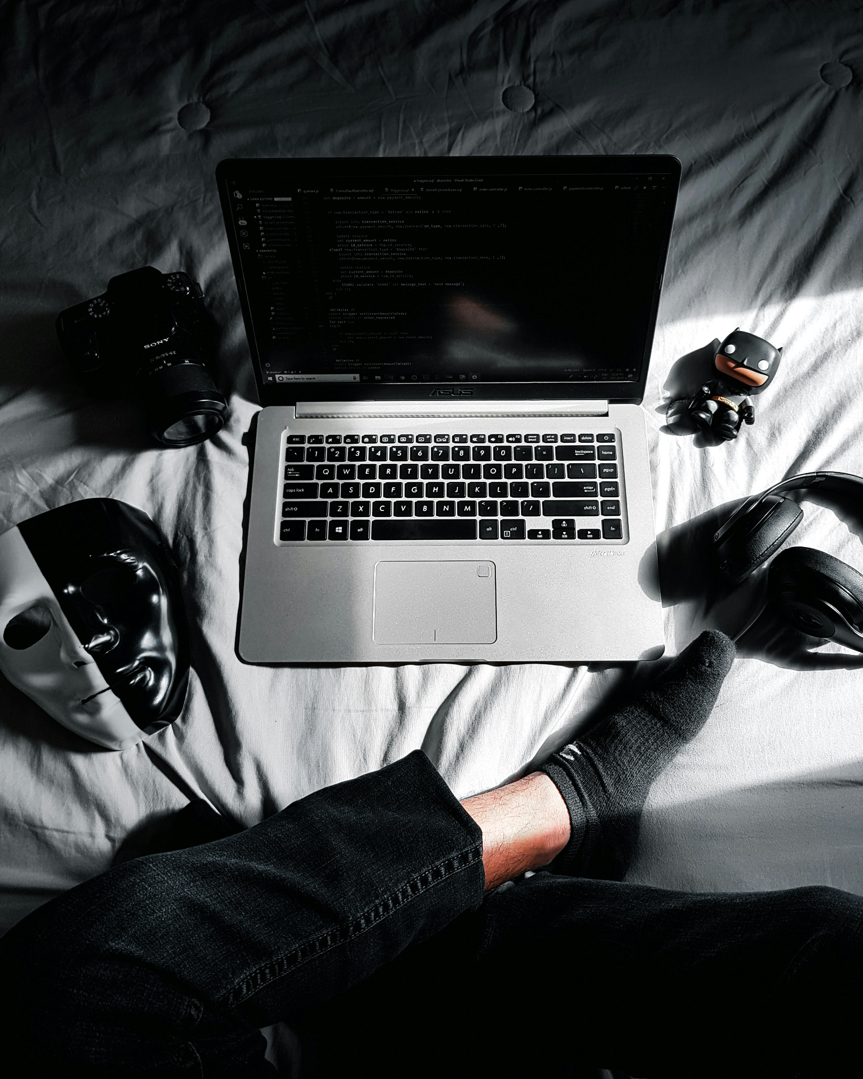 MacBook in middle of camera, action camera, mask, and headphones on bed