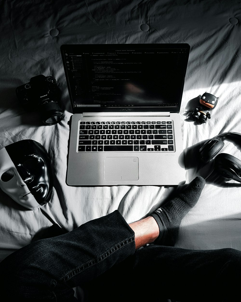 MacBook in middle of camera, action camera, mask, and headphones on bed