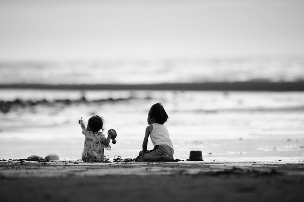 grayscale photography of two girls sitting on shore