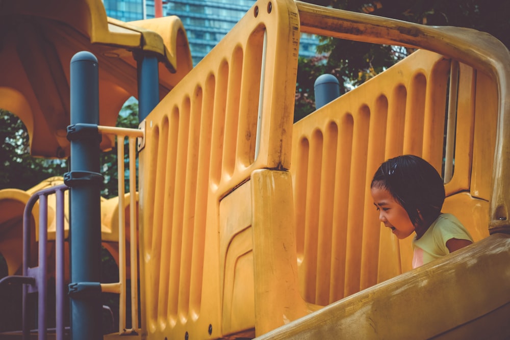 girl playing on yellow slide during daytime