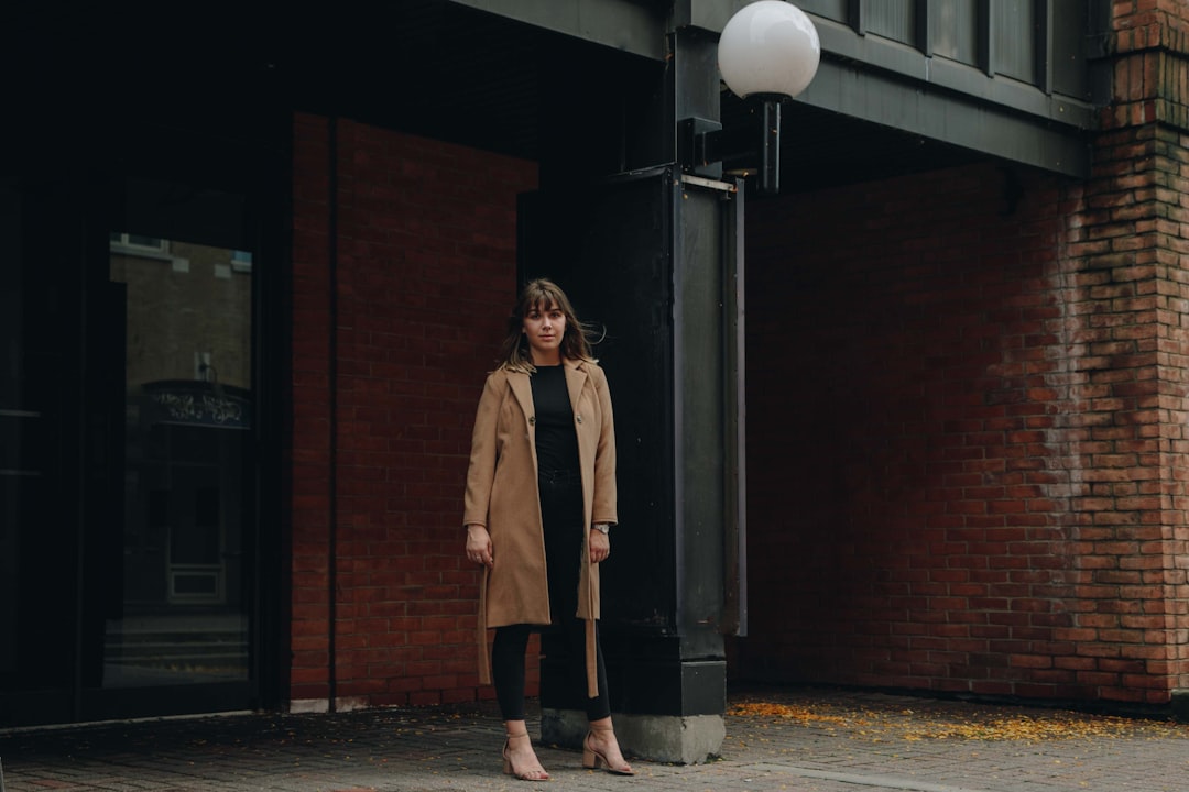 woman in brown trench coat stands in front of glass door