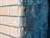 A close-up view of a corner between two walls, one covered with unfinished plaster and the other with brickwork. The plaster appears rough and uneven, with visible textures and imperfections. The bricks are neatly arranged, displaying a light orange color.