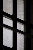 A close-up view of a window with a mesh screen, creating a grid-like pattern that contrasts with the light coming through the glass panes.