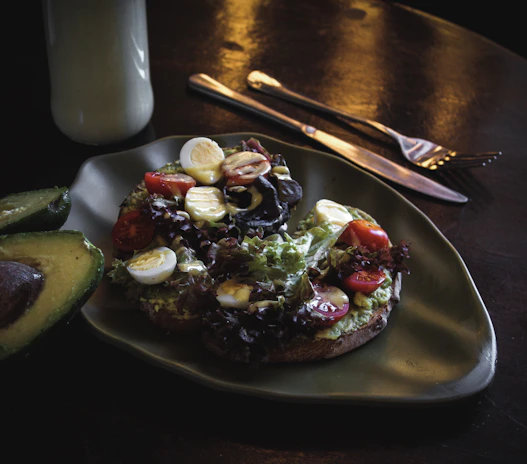 Close-up of a vibrant avocado toast topped with cherry tomatoes and microgreens on a rustic wooden table.