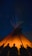 A warm glowing tipi lit from inside against a twilight sky.