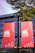 Two red banners hang outdoors from a street lamp post, featuring intricately designed cityscapes and text in both English and Chinese, promoting an event titled 'International Culture Week'. The background includes the facade of a modern building and overhanging green tree branches.