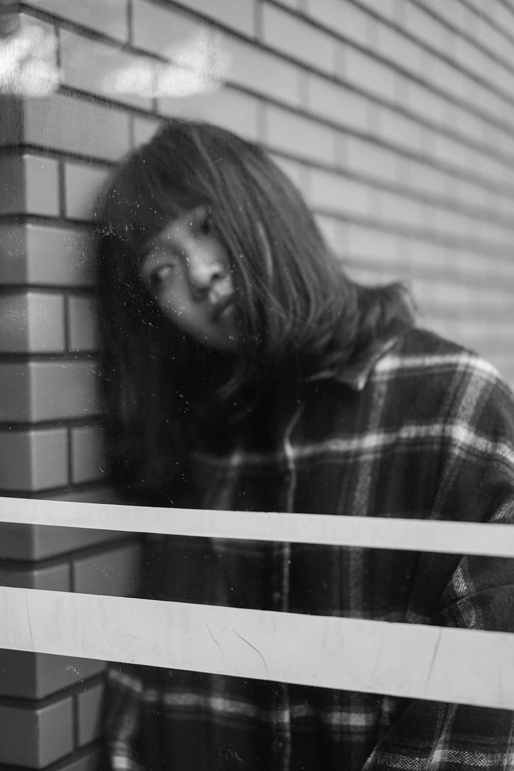 grayscale photography of woman leaning on brick wall