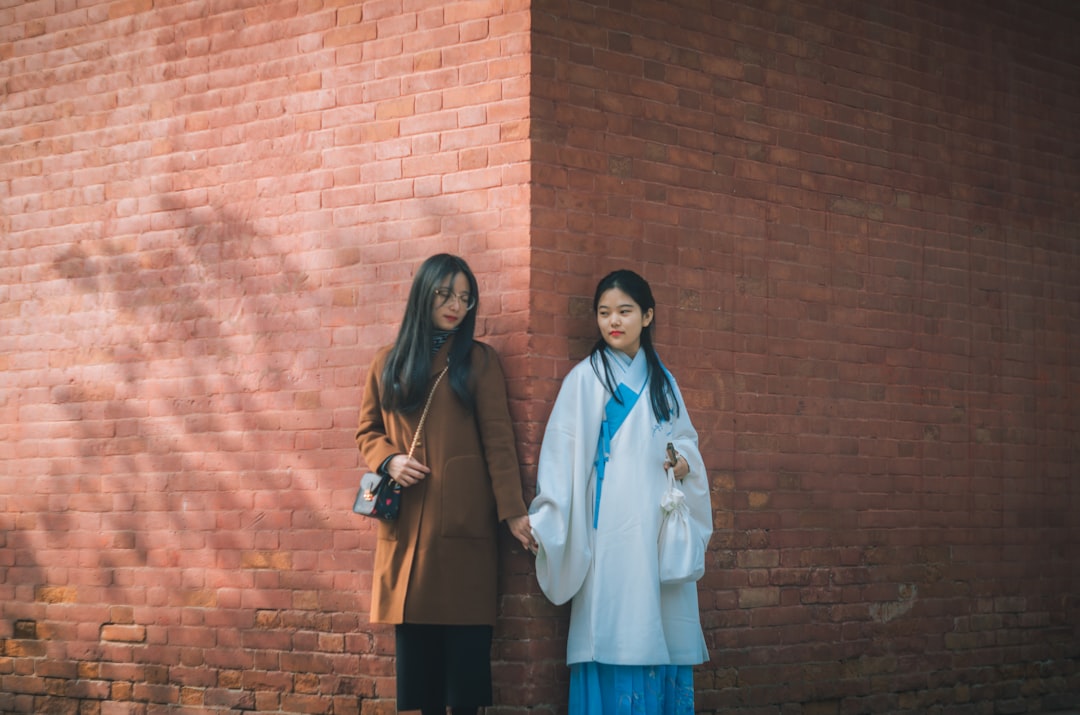 two woman holding hands while leaning on wall