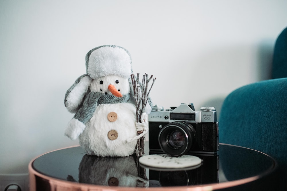 black and gray camera beside snowman doll on table