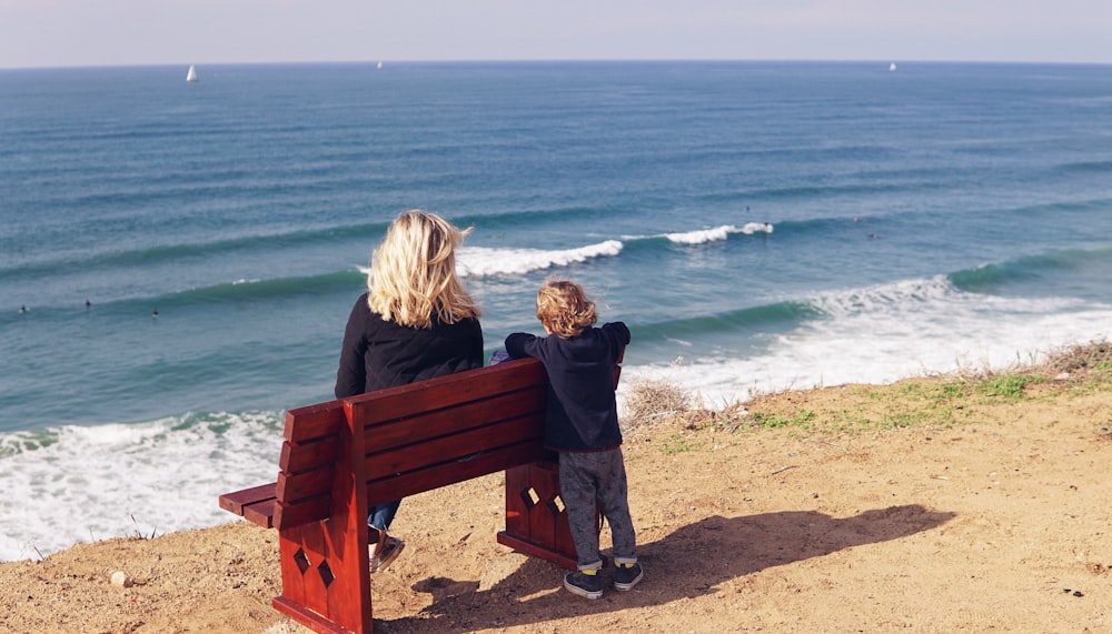 woman sitting on bench near boy standing at the back