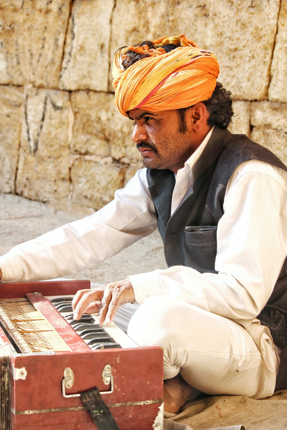 man sitting on ground playing harmonium