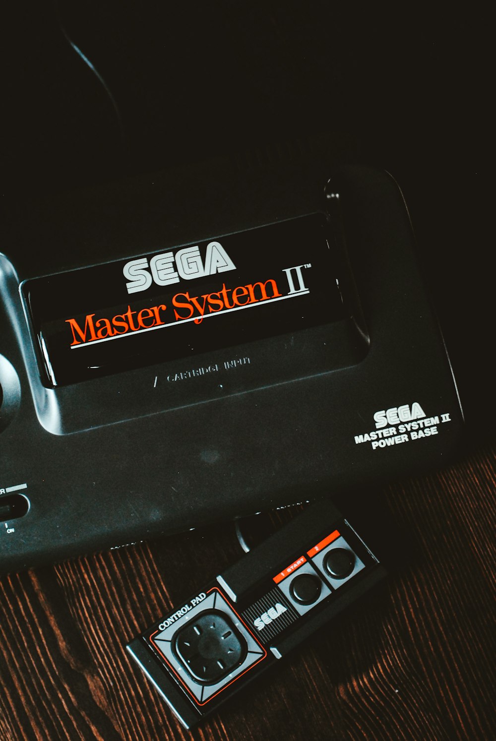 갈색 나무 표면에 검은색 Sega Master System II 장치