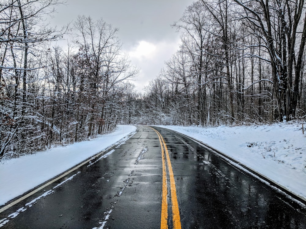 empty highway with solid double yellow line in between snow covered ground at daytime