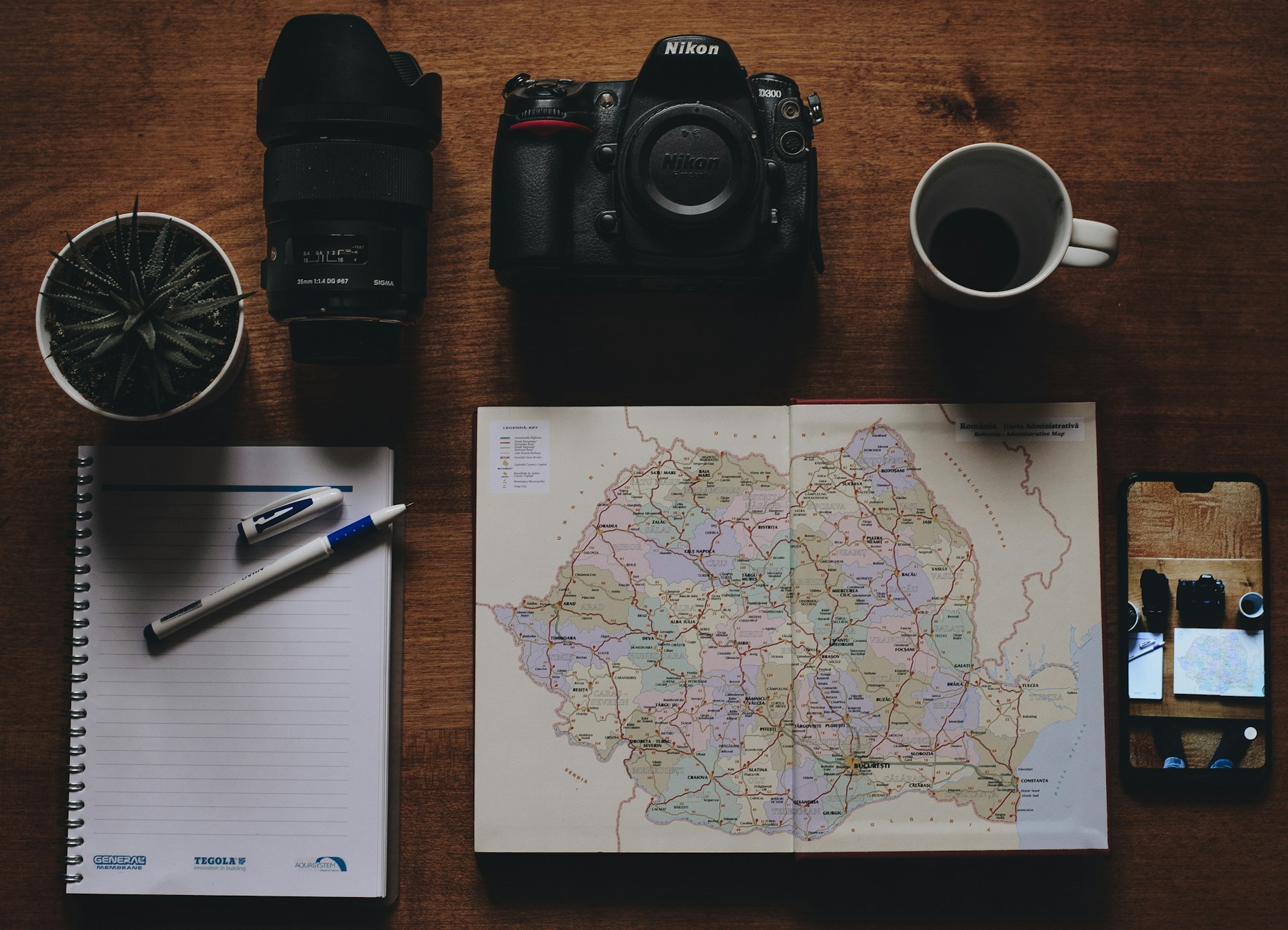 black Nikon DSLR camera beside white mug and map on brown table