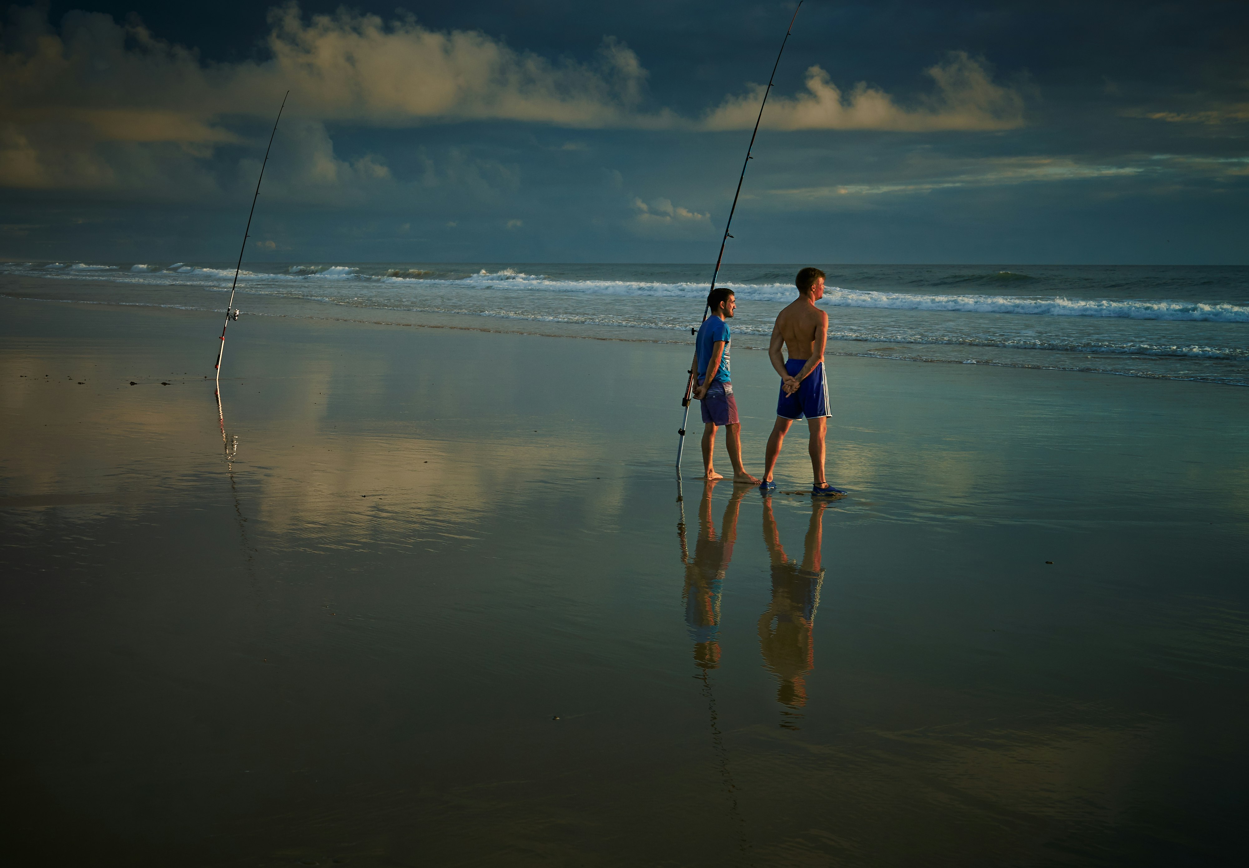 two boy standing beside fishing rod stump on shoreline at daytime