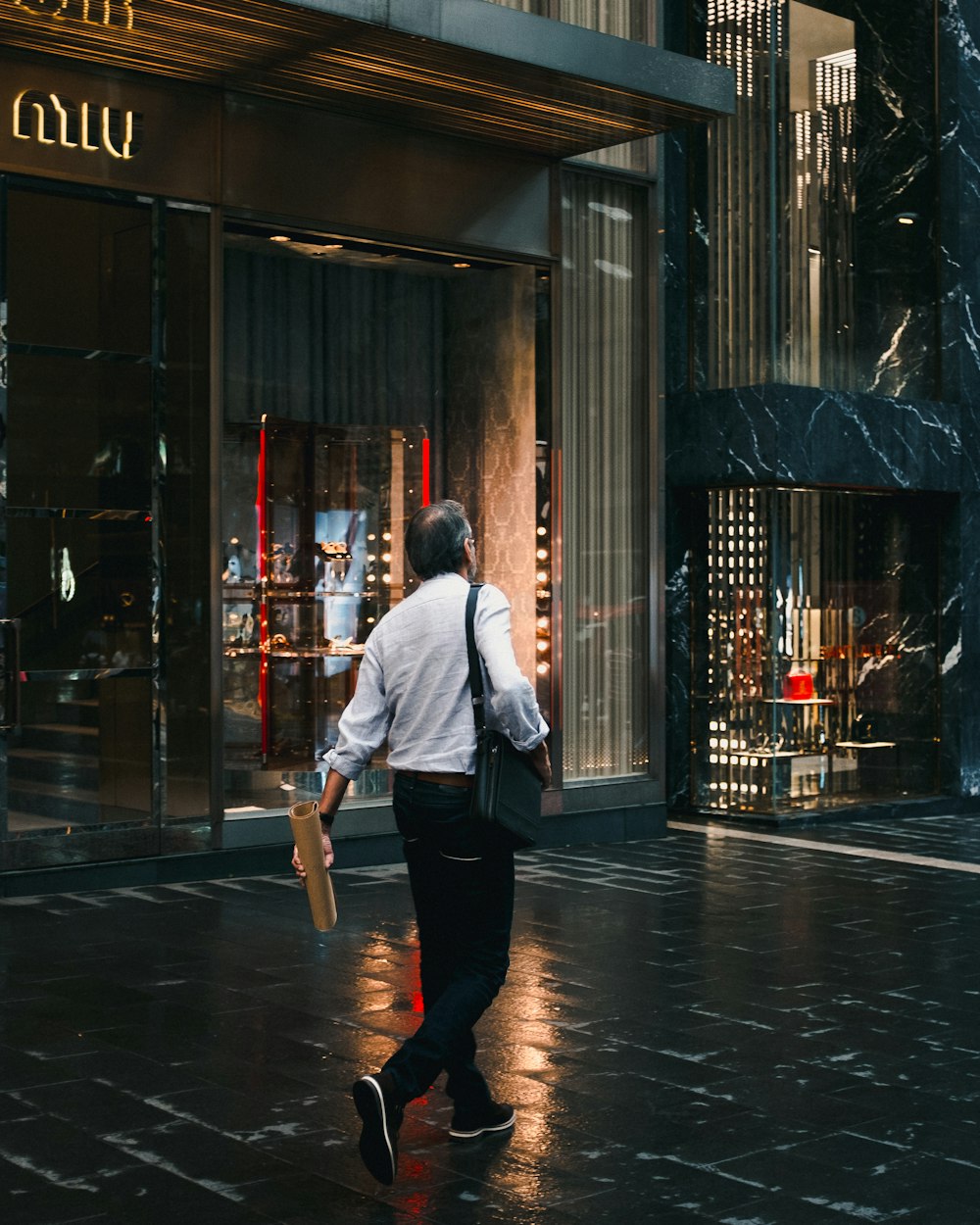 man holding brown tube walking on sidewalk