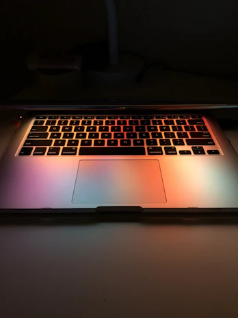 A laptop keyboard illuminated by natural light with a tech review notebook nearby.