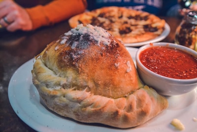 Close-up of a golden calzone oozing with melted cheese and savory fillings on a clean white plate.