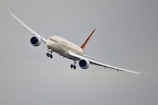 A commercial airplane is flying at a slight bank in a clear sky. The aircraft has a sleek design with long wings and powerful jet engines, positioned below each wing.