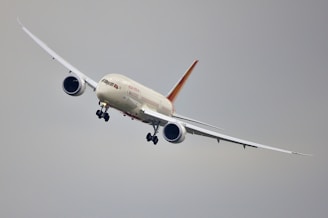 A commercial airplane is flying at a slight bank in a clear sky. The aircraft has a sleek design with long wings and powerful jet engines, positioned below each wing.