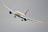 A commercial airplane is flying at a slight bank in a clear sky. The aircraft has a sleek design with long wings and powerful jet engines, positioned below each wing.