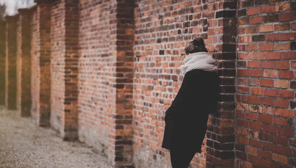 woman leaning on red brick wall